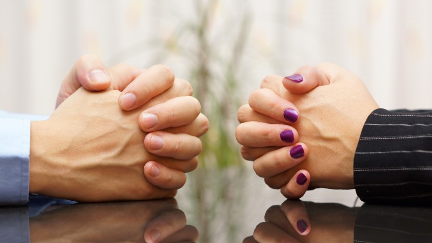 Man and woman sits at a desk with hands clasped. marital problem