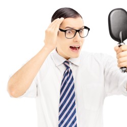 Young worried man checking for thinning hair in the mirror