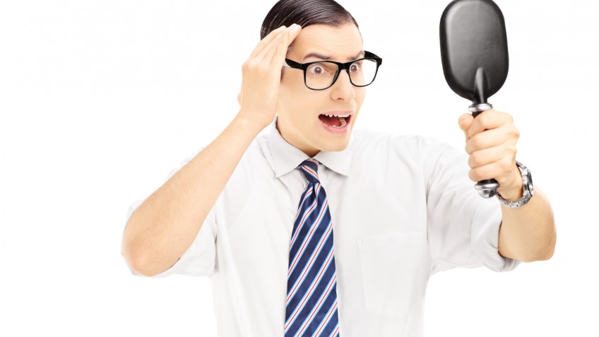 Young worried man checking for thinning hair in the mirror