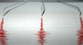 A closeup of a seismograph machine needle drawing a red line on graph paper depicting seismic and eartquake activity on an isolated white background