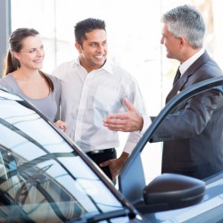 mature salesman showing new car to a couple in showroom