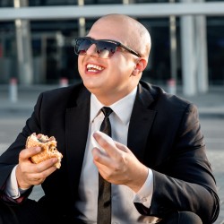 Businessman or banker working with laptop and having snack with burger outside the airport or contemporary building