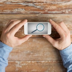 business, education, people and technology concept - close up of male hands holding smartphone with magnifying glass picture on screen at table