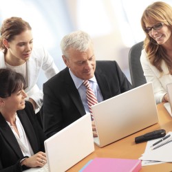 Portait of businesswomen and businessman sitting at office desk in front of computer and working together on presentation.