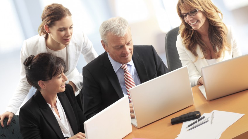 Portait of businesswomen and businessman sitting at office desk in front of computer and working together on presentation.