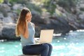 Freelance woman working in vacation on the phone on the beach with the sea in the background