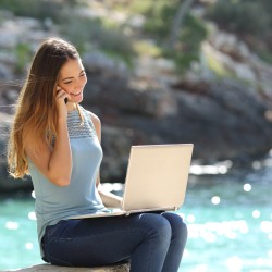 Freelance woman working in vacation on the phone on the beach with the sea in the background