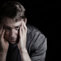 Closeup front view of mature man with head down, touching his temples, while displaying depression on black background