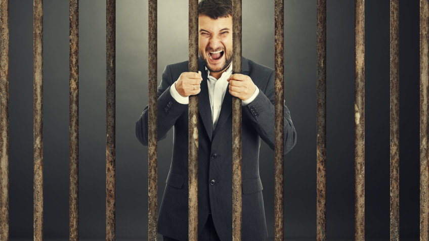 angry screaming businessman behind the prison cell over dark background