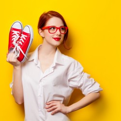Beautiful redhead girl in white shirt with gumshoes on yellow background.