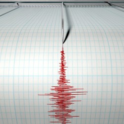 A closeup of a seismograph machine needle drawing a red line on graph paper depicting seismic and eartquake activity on an isolated white background