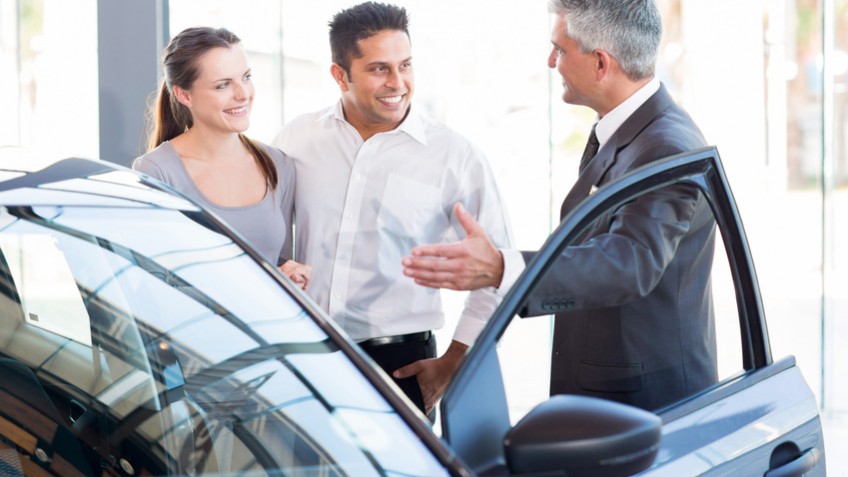mature salesman showing new car to a couple in showroom