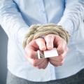 A debt concept or metaphor - a businesswoman with tied up hands holding a credit card.