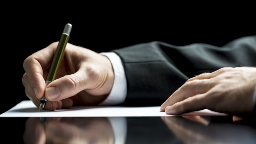 Businessman writing a letter, notes or correspondence or signing a document or agreement, close up view of his hand and the paper